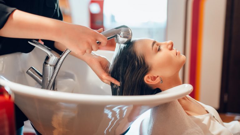 Hairdresser washes customer hair in basin